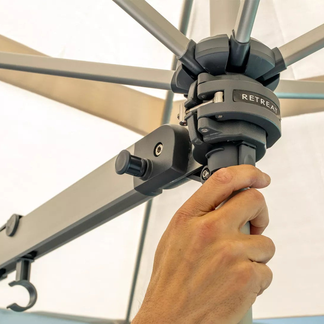 Hand adjusting a patio umbrella with a visible brand logo against a neutral background