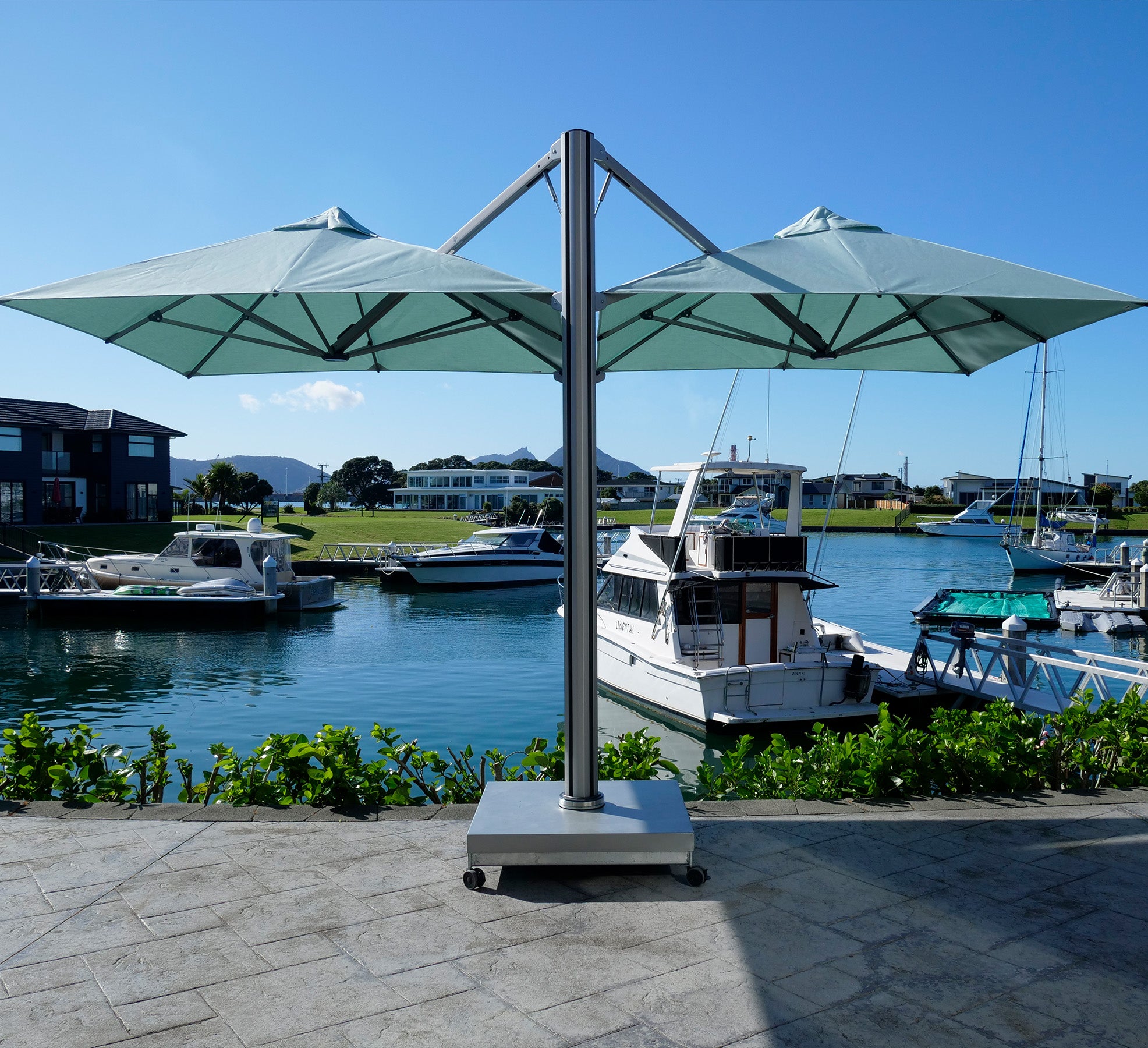 Large outdoor umbrella with a base on a dock with boats and a clear sky.