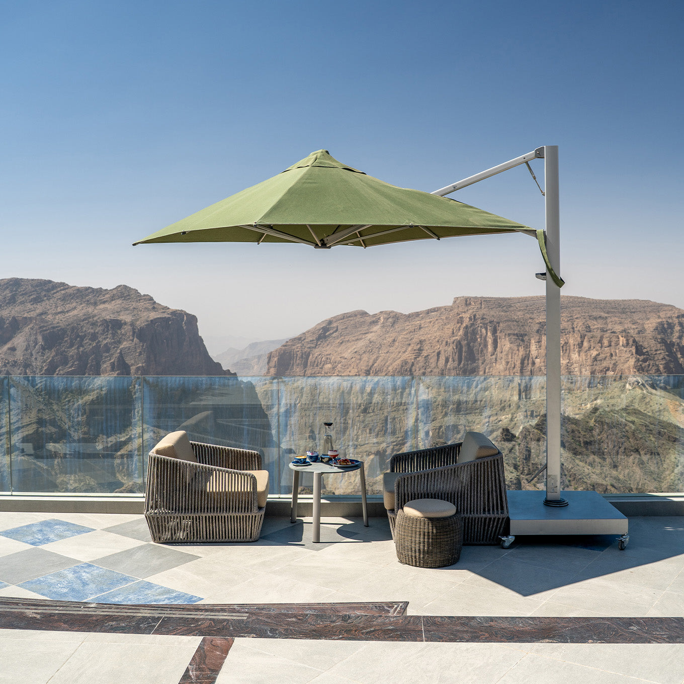 Outdoor patio set with a green umbrella and chairs on a terrace with a scenic view of mountains.