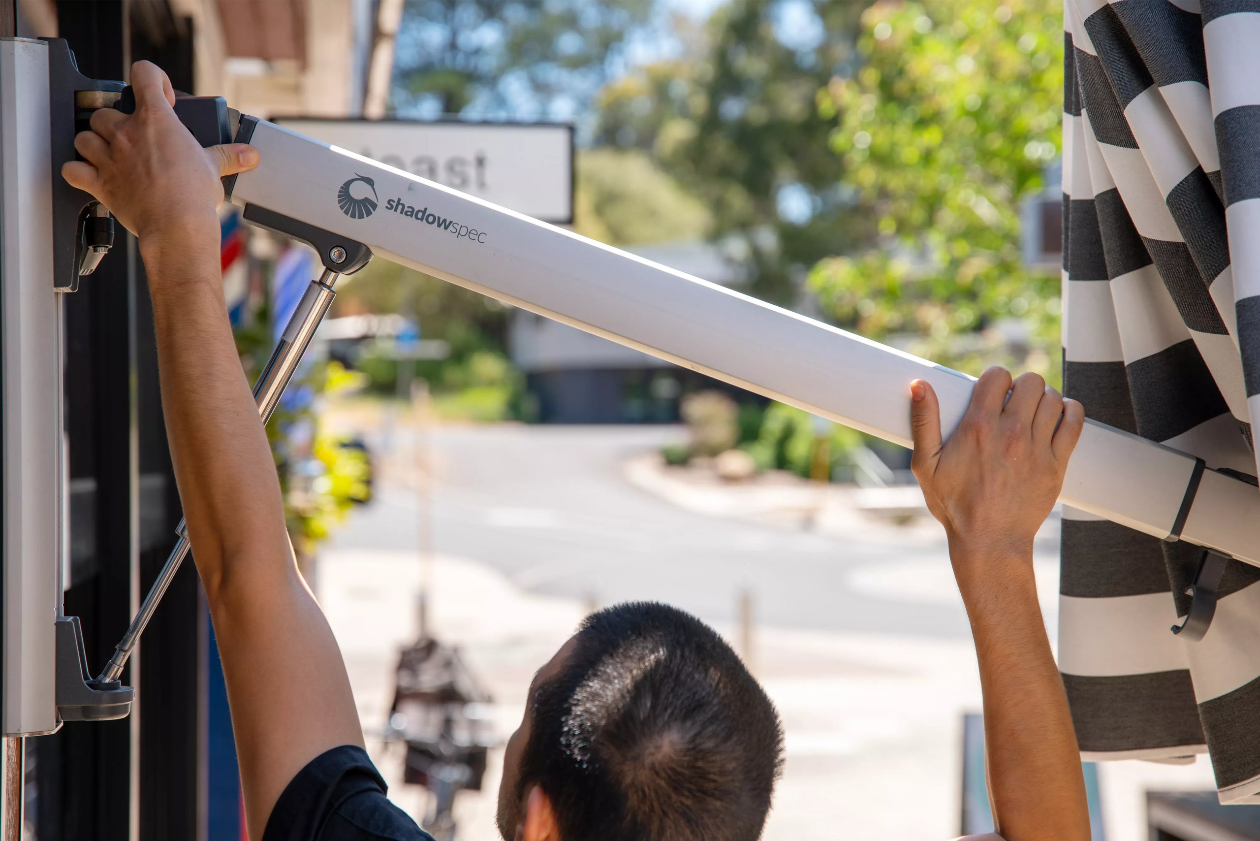 Person opening a wall mounted umbrella  outside a cafe against a blurred background