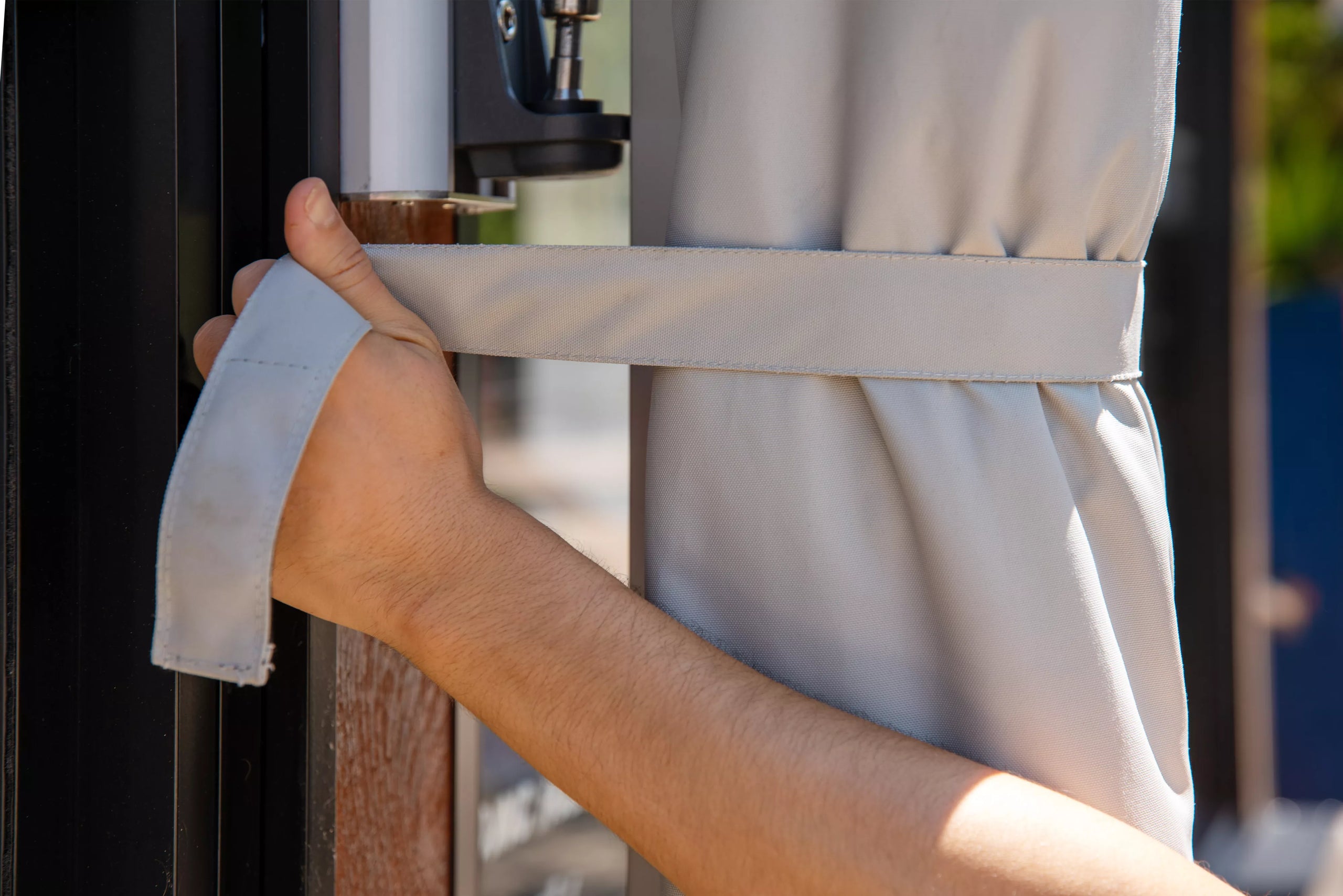 Person tying an umbrella cover to the wall, with a blurred background