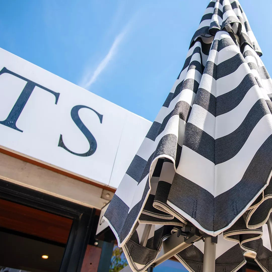 Black and white striped umbrella against a clear blue sky with a building and sign in the background.